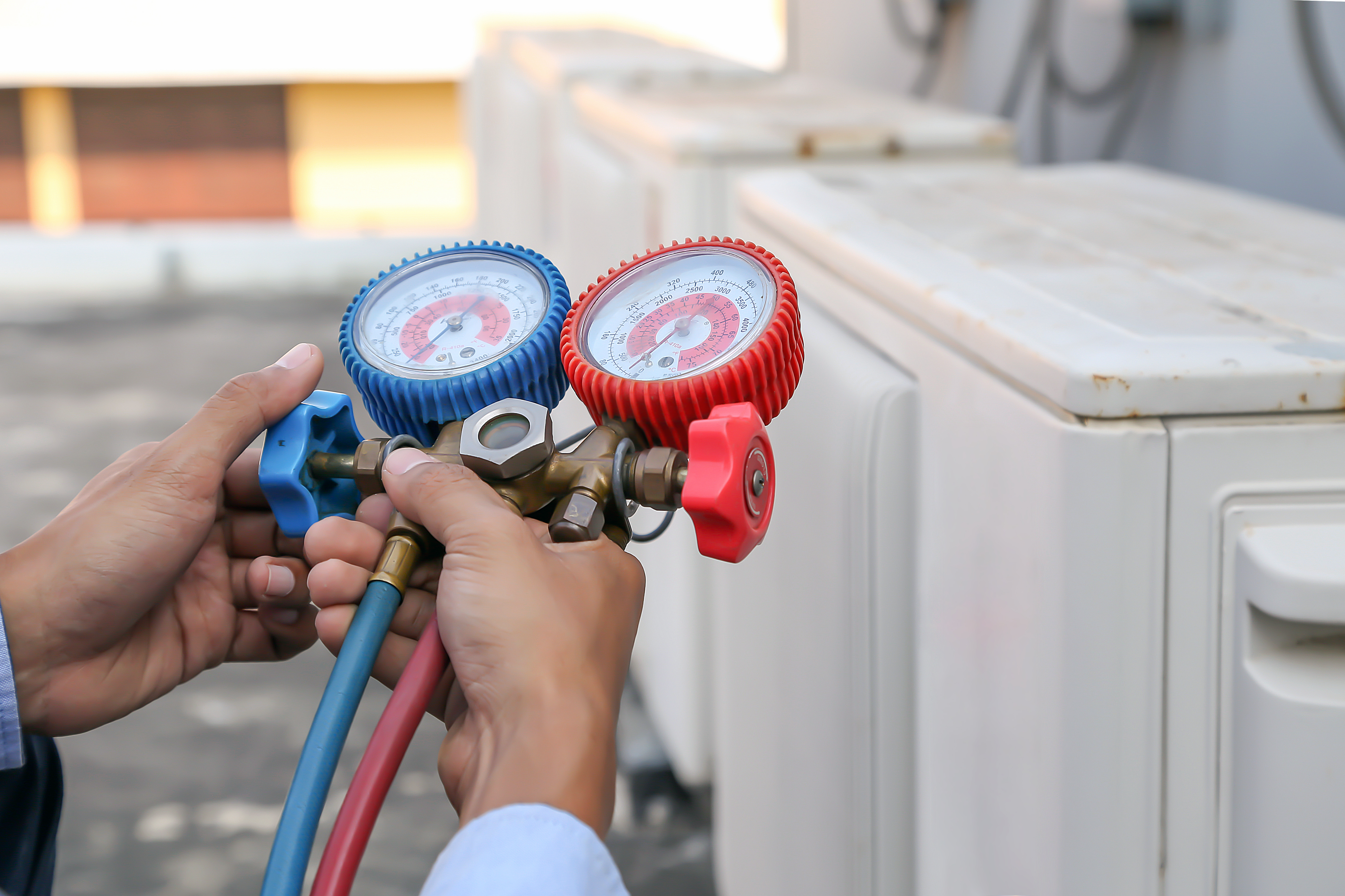 Technician using manifold gauge is measuring equipment for filling industrial factory air conditioners and checking maintenance outdoor air compressor unit.